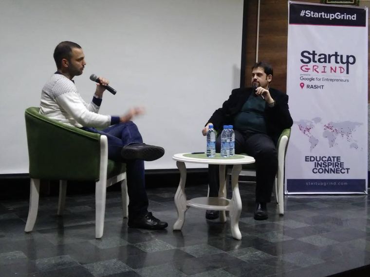 Two people in conversation on stage in front of a Startup Grind Rasht banner
